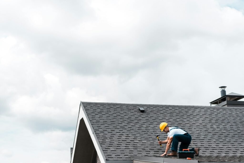repairman in helmet holding hammer while repairing roof | Kempthorne Roofing & Construction